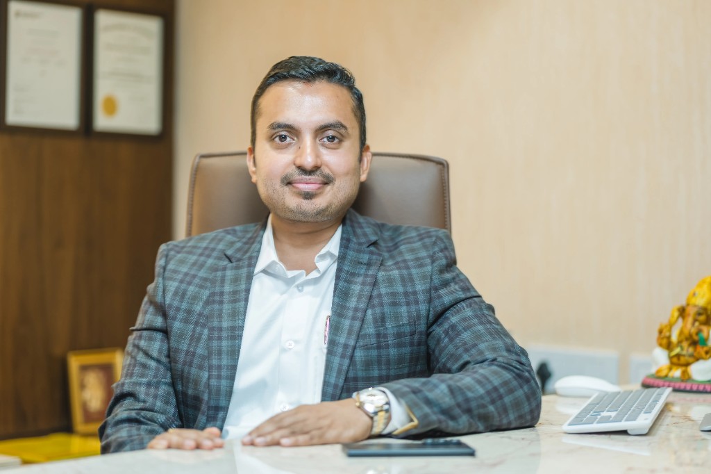 Vaishnav K. Sanil, Director of Nidhi Land Developers, seated at his desk in a grey plaid blazer